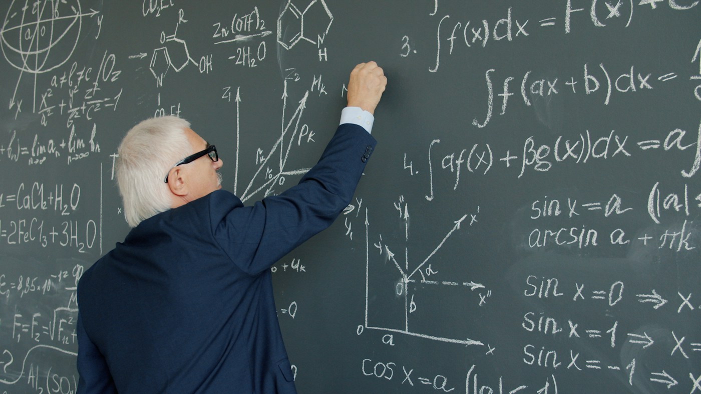 A teacher writing integrals and trigonometric identities on a chalkboard