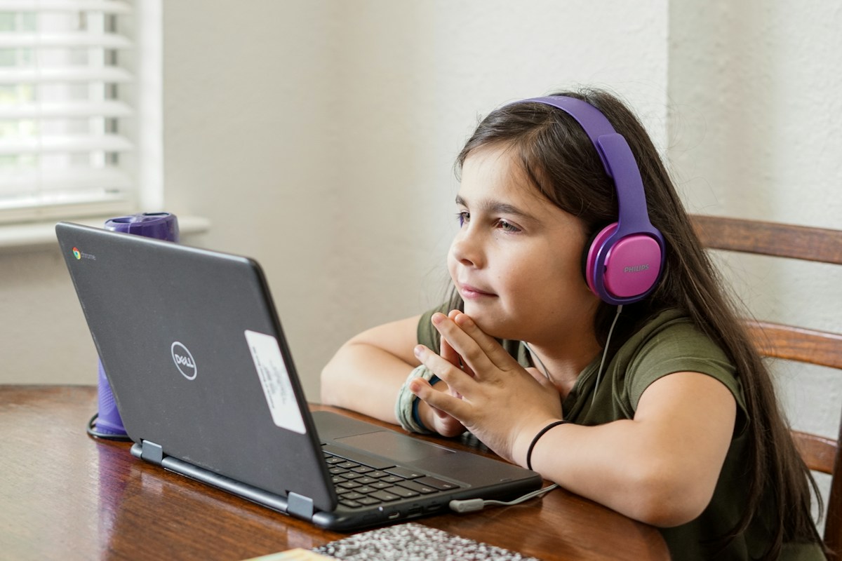 A student with headphones attending a live online class on her laptop
